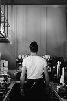 A barista working behind the counter in a café, captured in black and white.