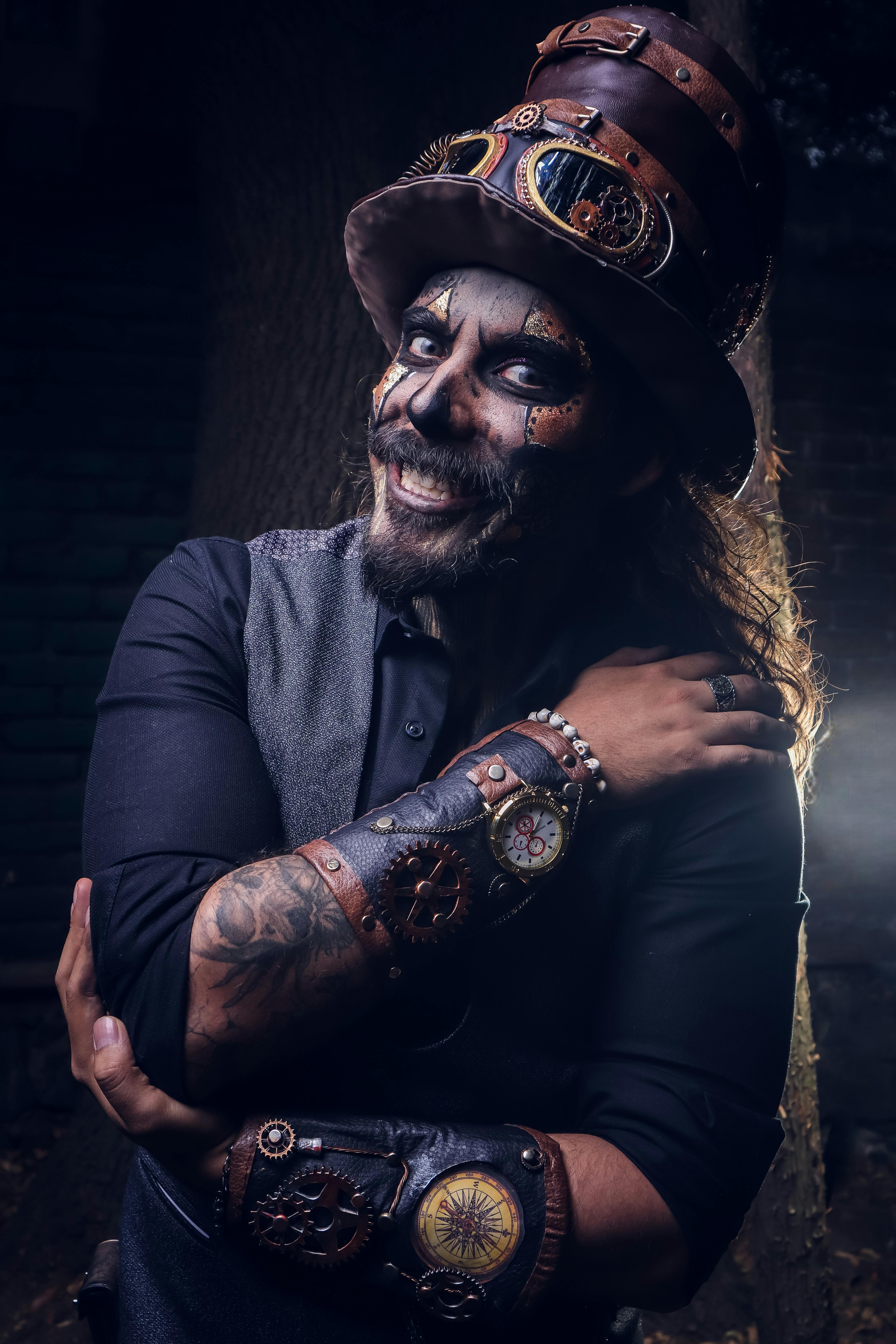 A steampunk performer in costume with makeup, gears, and a top hat, smiling confidently.