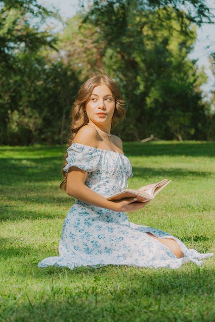 A young woman in a sundress enjoys reading outdoors in a lush green park.