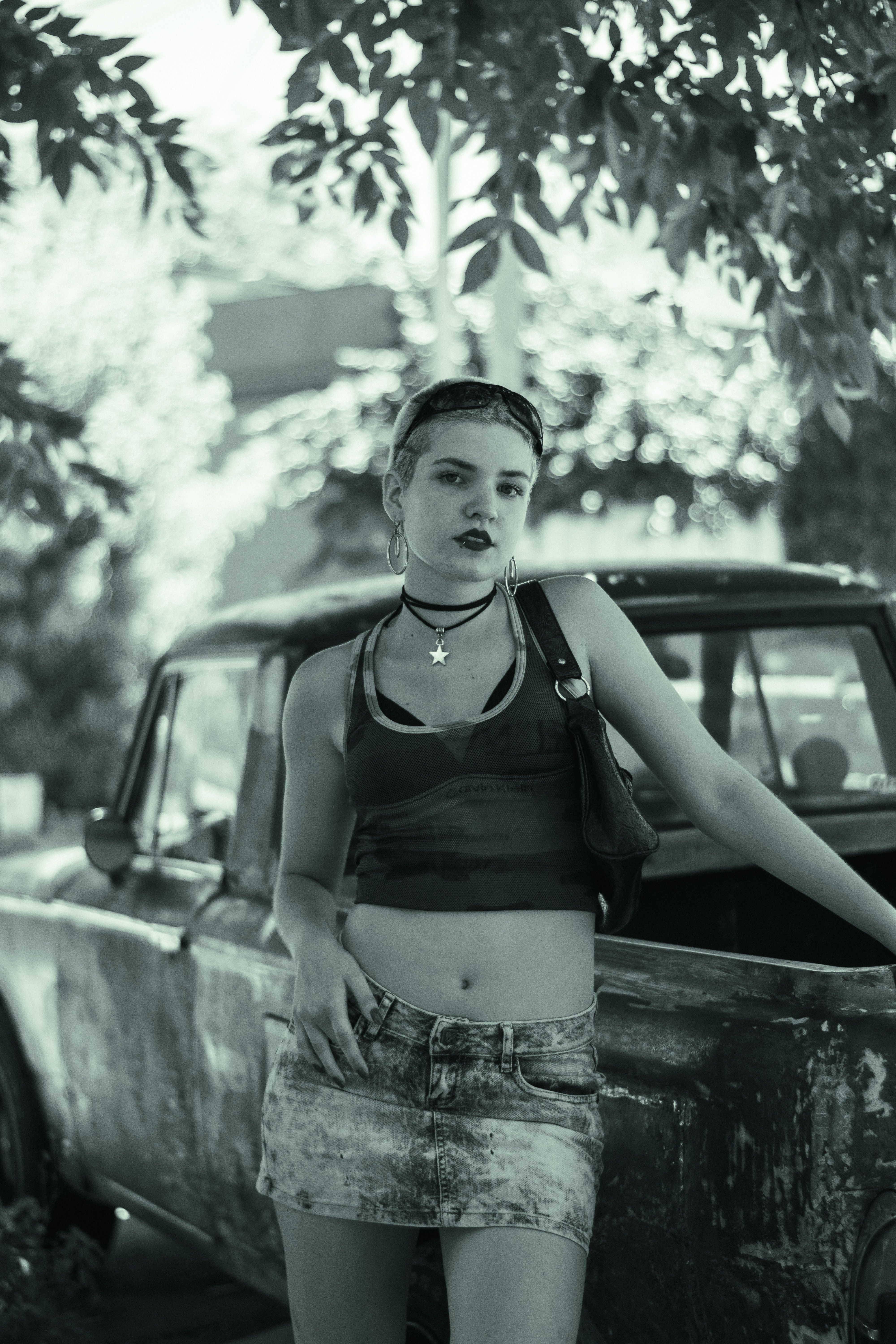 A fashionable young woman stands confidently next to a vintage truck on a sunny day.