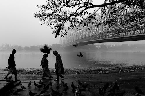 A black and white photo of people walking by a bridge