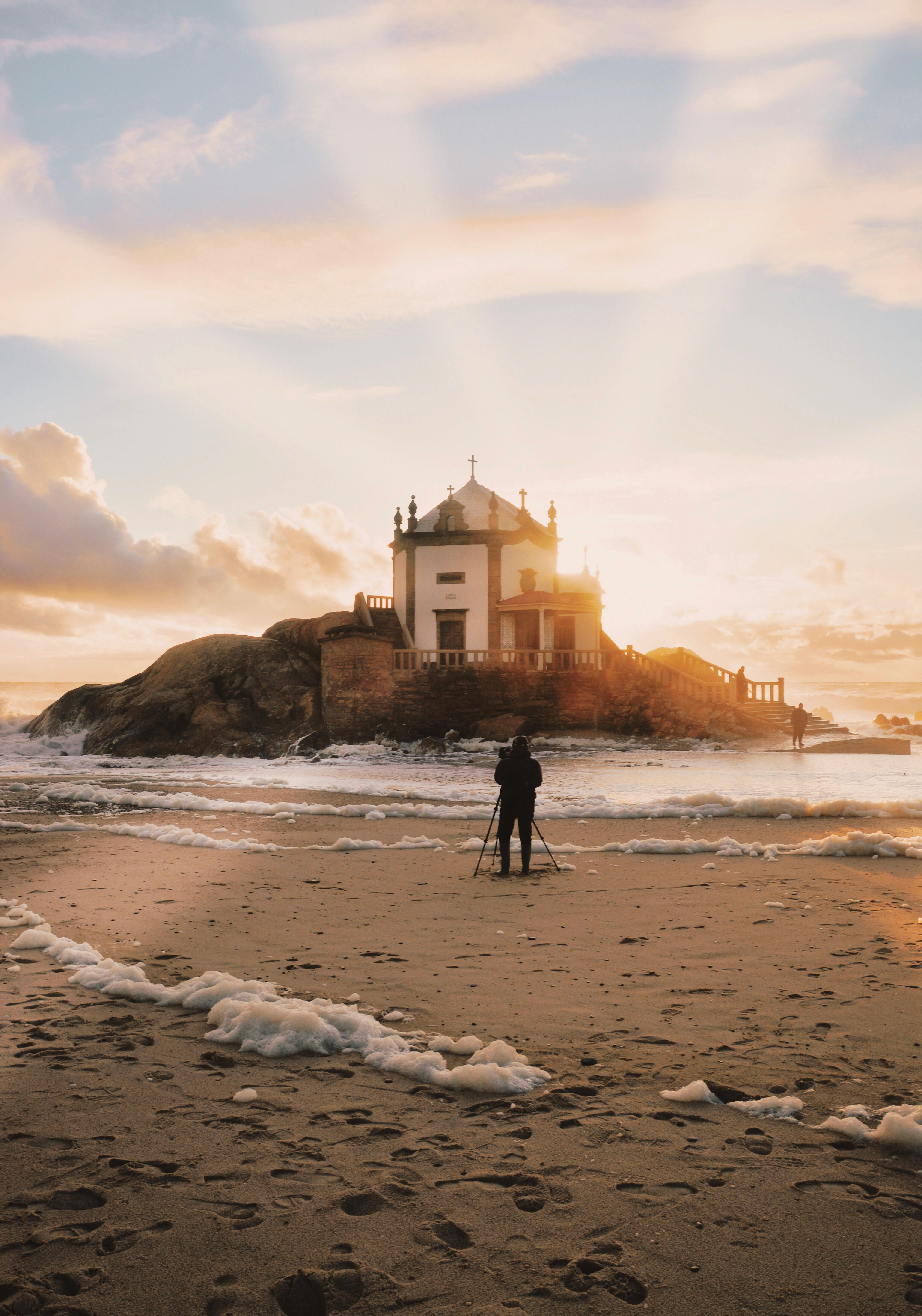 person standing near sea shore overlooking island during golden hour