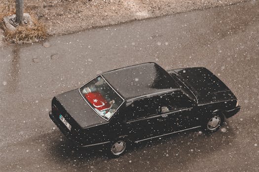Aerial view of a vintage black car driving on a snowy street in Ankara, Türkiye, with the Turkish flag visible.