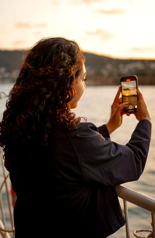 Free Woman takes a sunset photo on her smartphone while standing by a railing. Stock Photo