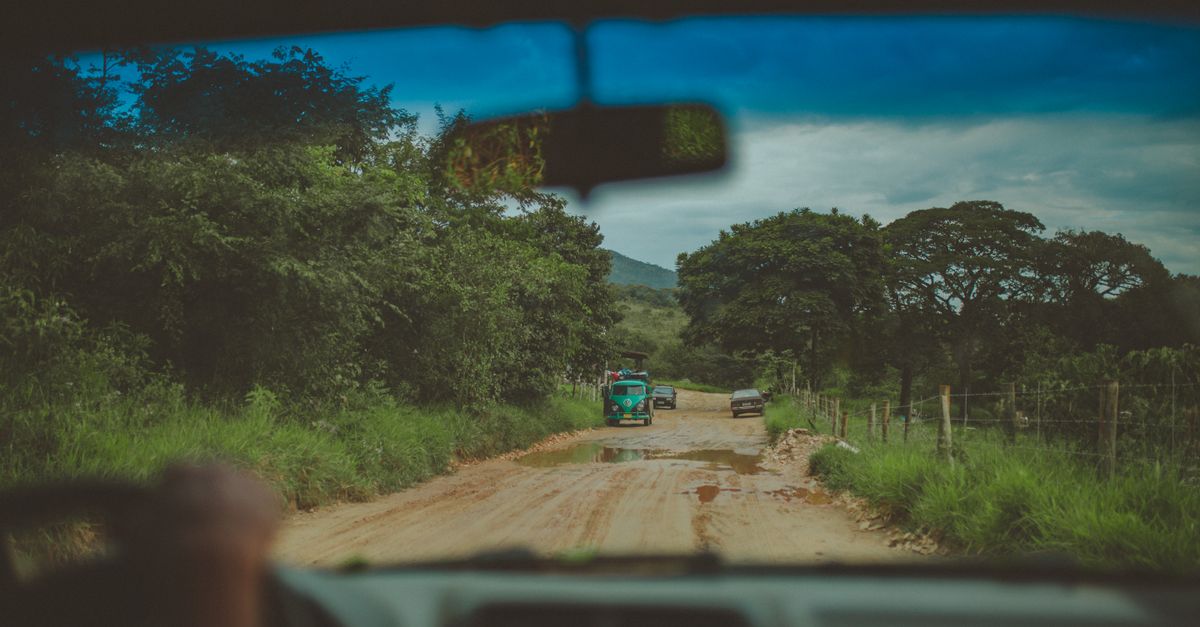 Experience a scenic drive on a rural dirt road, surrounded by lush greenery and overcast skies.