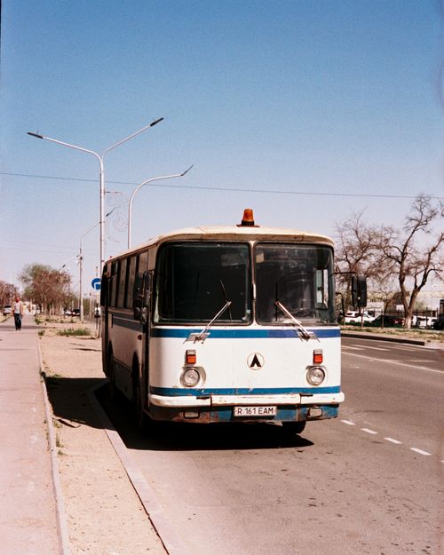 Free A vintage bus is parked on a sunny city street alongside bare trees. Stock Photo