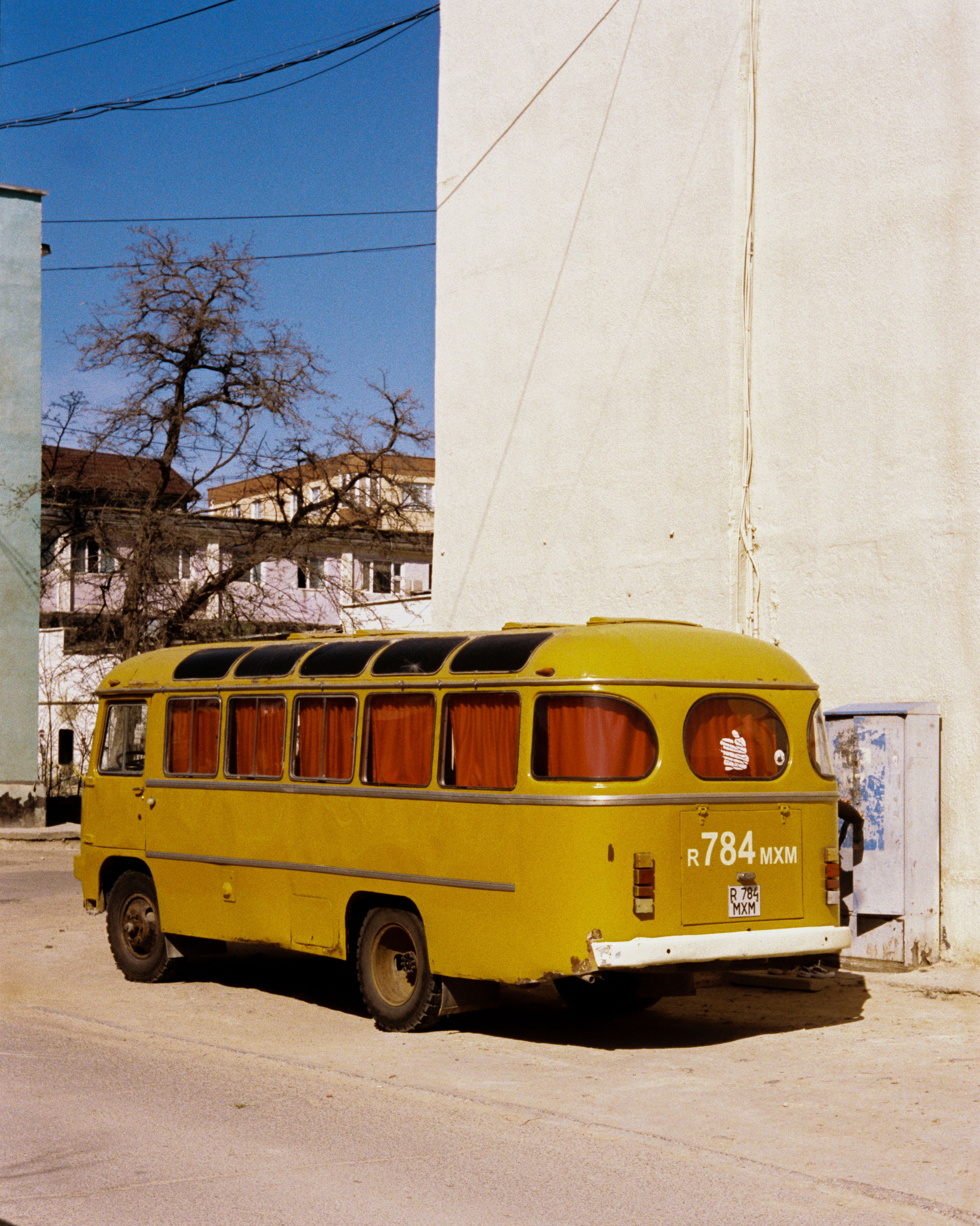 A classic yellow bus parked on a sunny street corner with urban architecture.