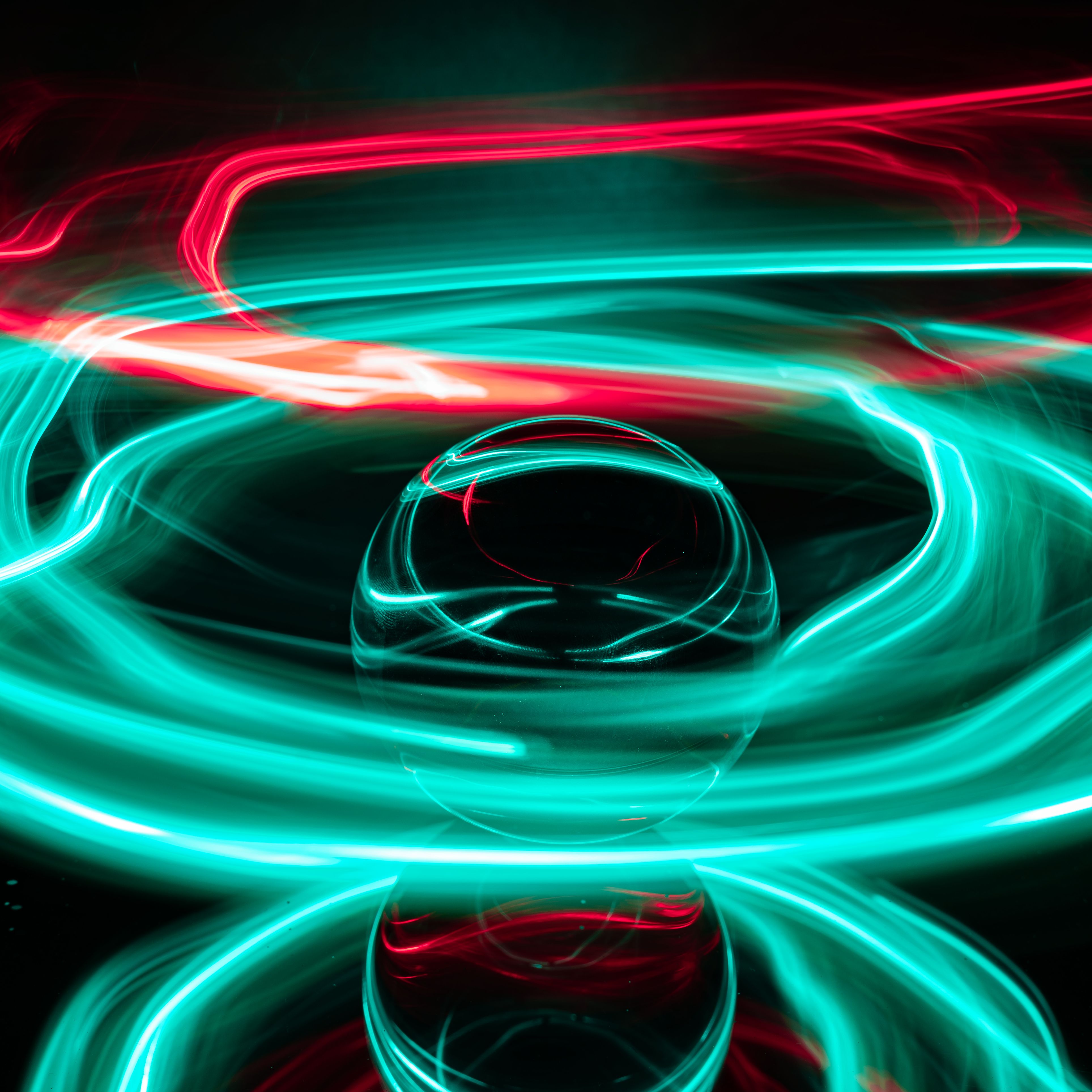 Dynamic long exposure of vibrant green and red light trails swirling around a glass sphere on black background.