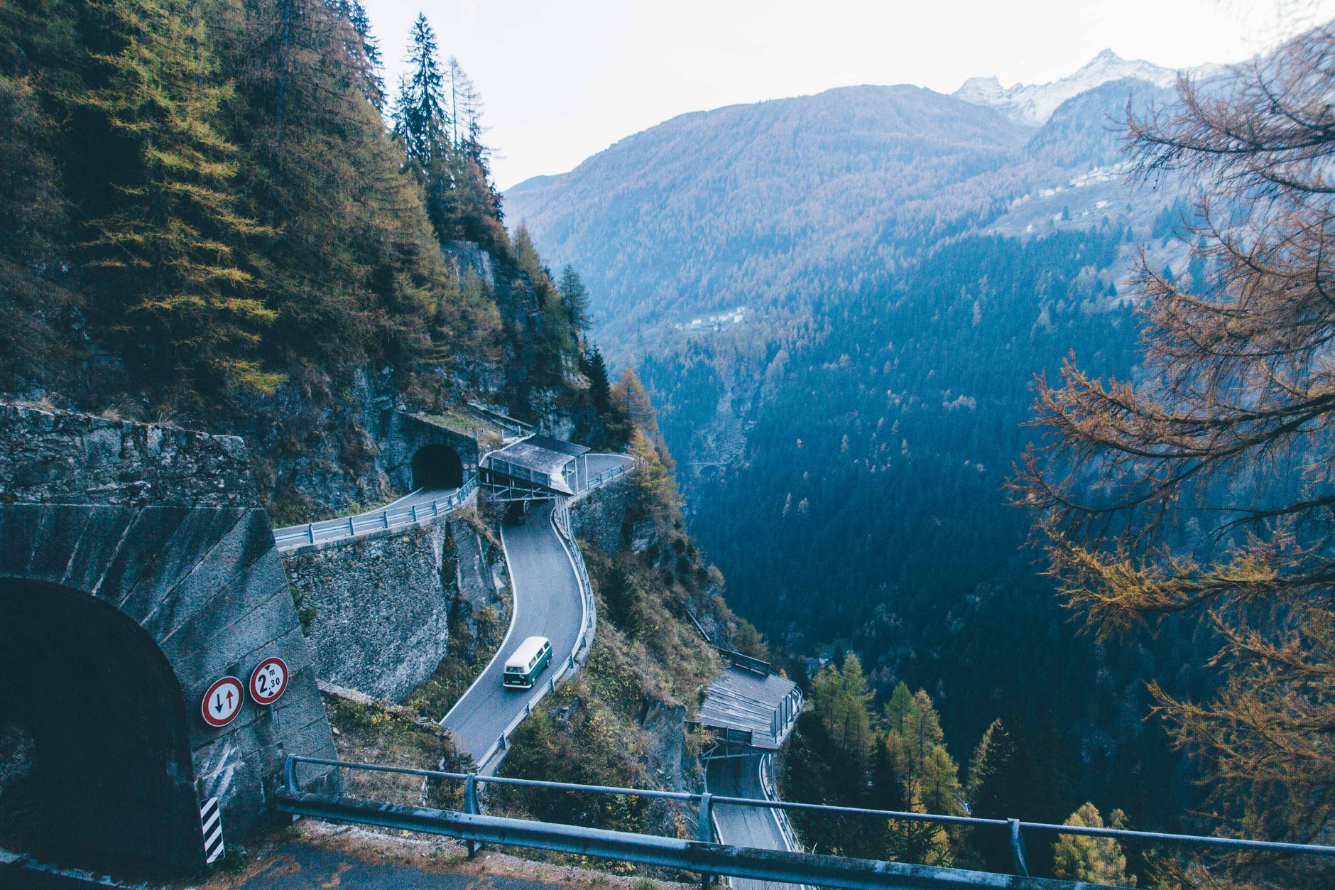 A breathtaking high angle view of a mountain road with a tunnel and a van driving through a pine tree forest.