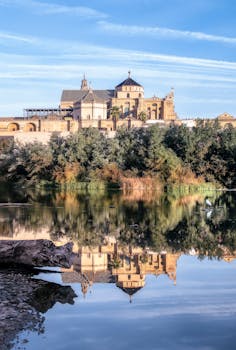 Stunning reflection of the Mosque-Cathedral of Córdoba on the Guadalquivir River, capturing its historic architecture.