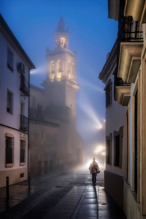 Free A mysterious foggy street in Córdoba, Spain with a lit bell tower and a lone walker. Stock Photo