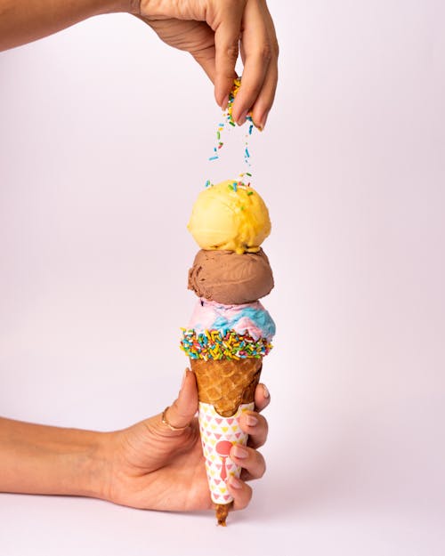 A person holding up three ice cream cones with sprinkles