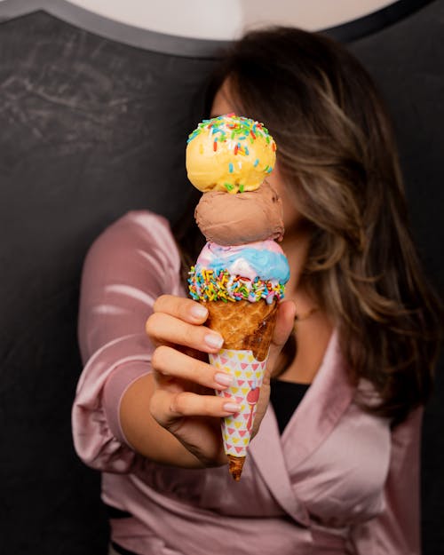 A woman holding up an ice cream cone with three different flavors