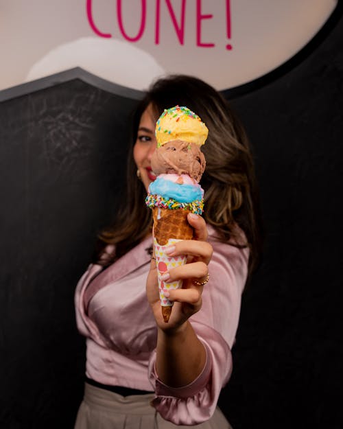 A woman holding up a cone with three different flavors