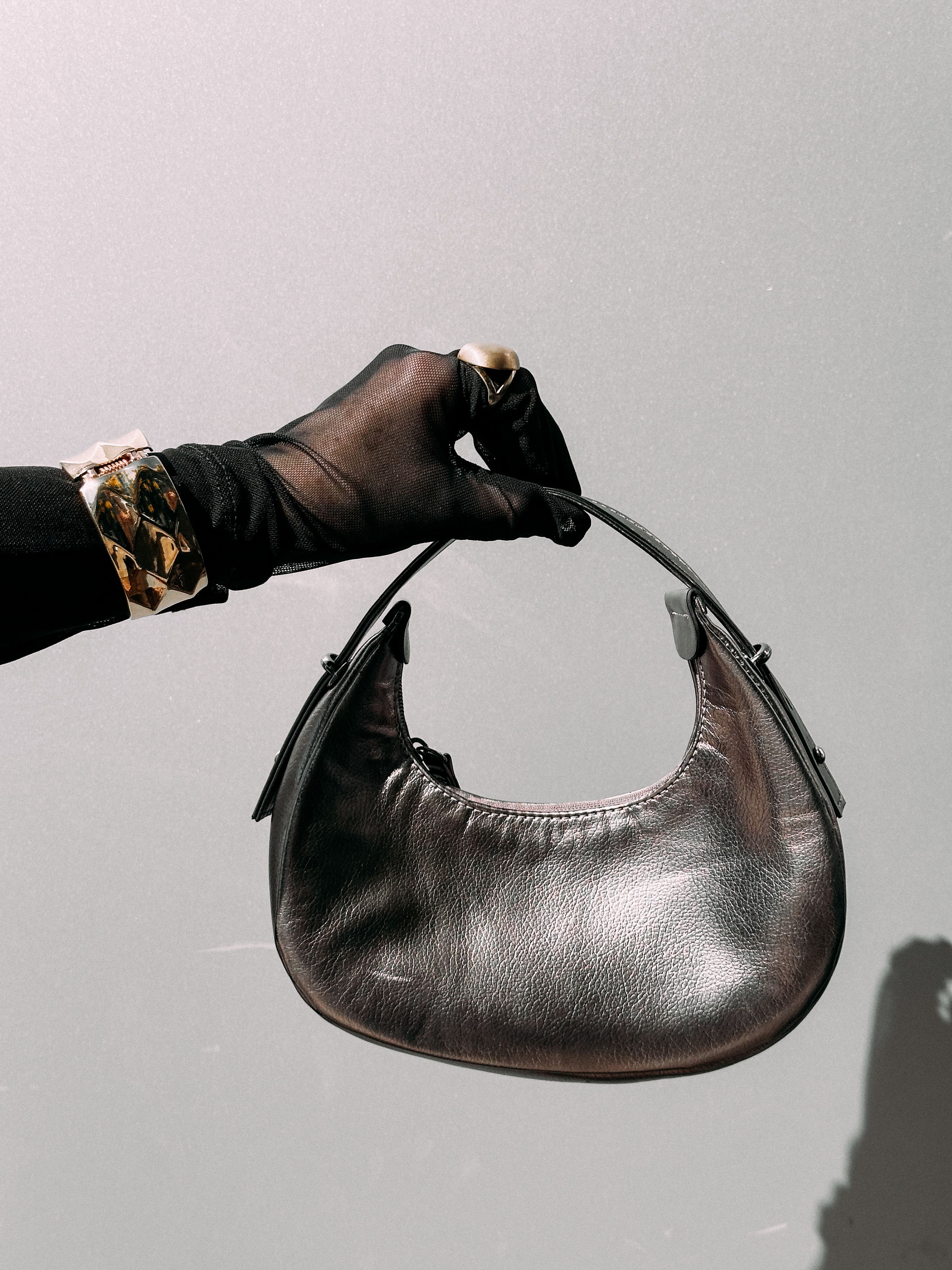 Close-up de uma mão com luva segurando uma bolsa de couro prateada, destacando acessórios de moda elegantes.