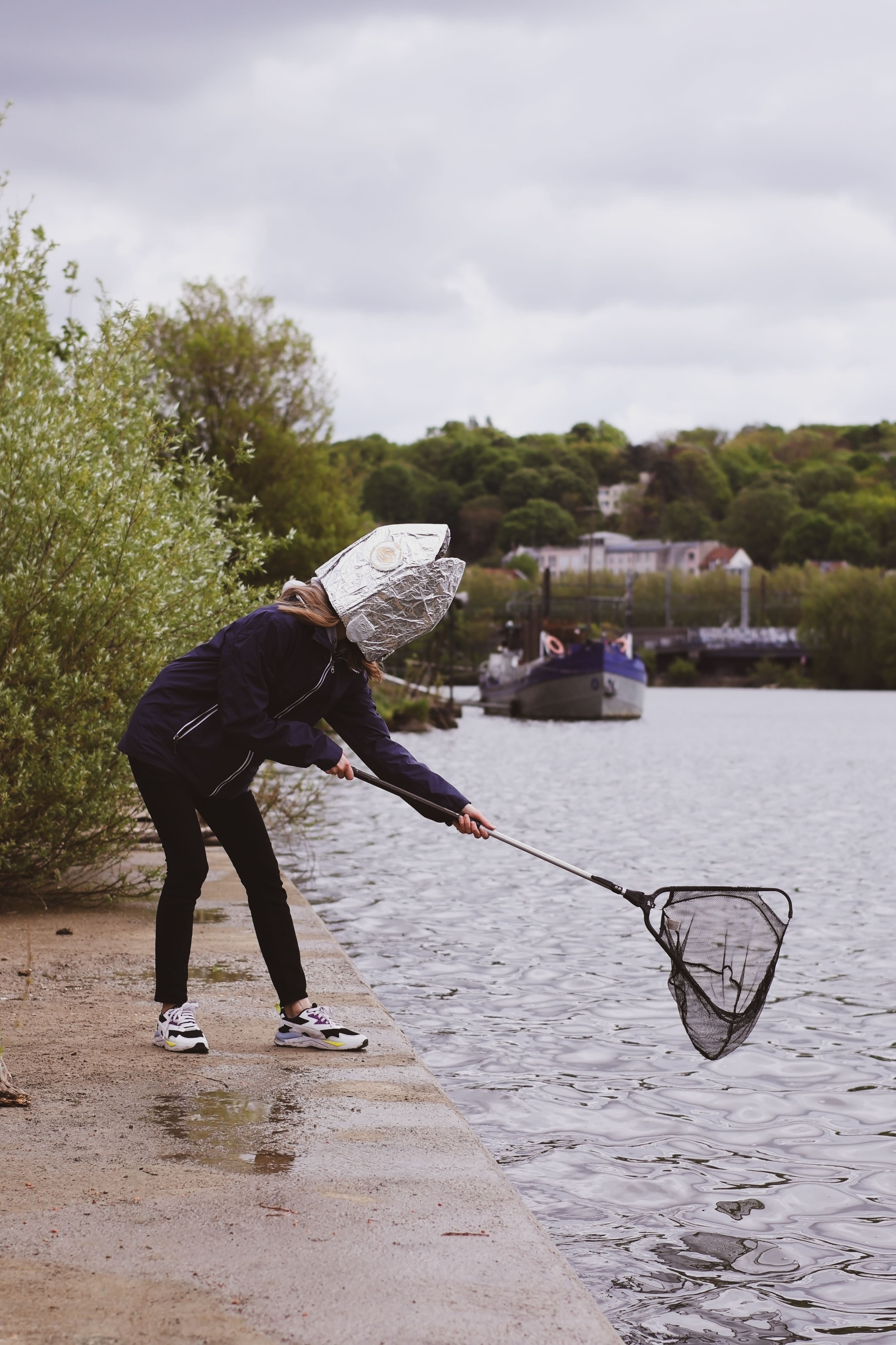 Woman Wearing a Tin Foil Fish Hat Using a Fishing Net on a Riverbank ...
