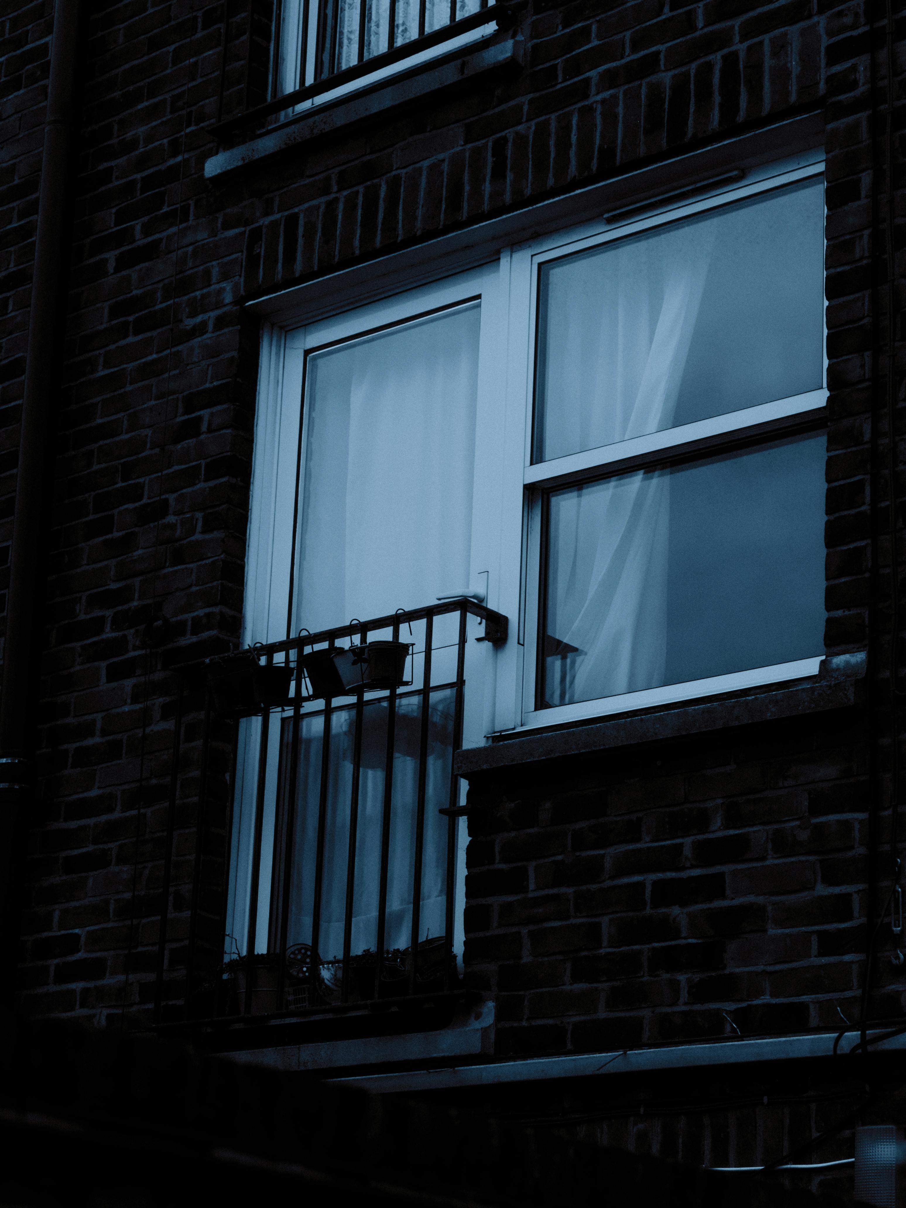 A dark and moody photograph of a residential building's window with curtains, taken at night.