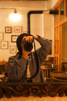 Woman taking a selfie in a cozy, warm-toned cafe with soft lighting and wooden accents.