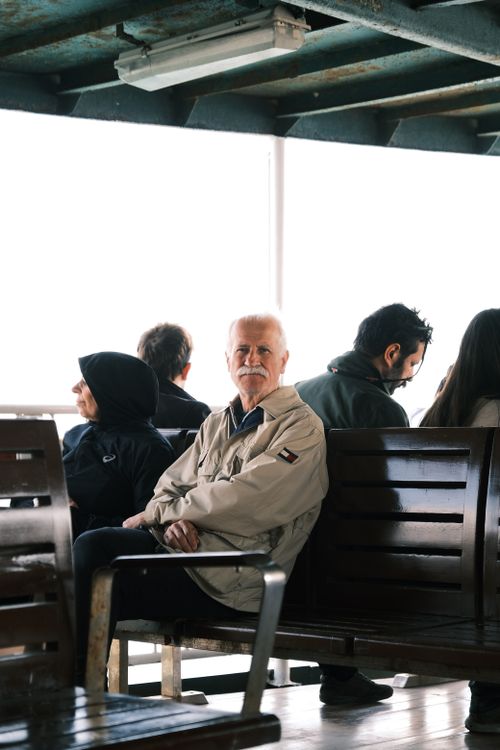 Free An elderly man sitting on a ferry surrounded by other passengers, creating a travel scene. Stock Photo