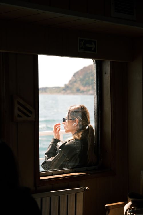 Free Woman wearing sunglasses, gazing through ferry window at scenic sea view. Stock Photo