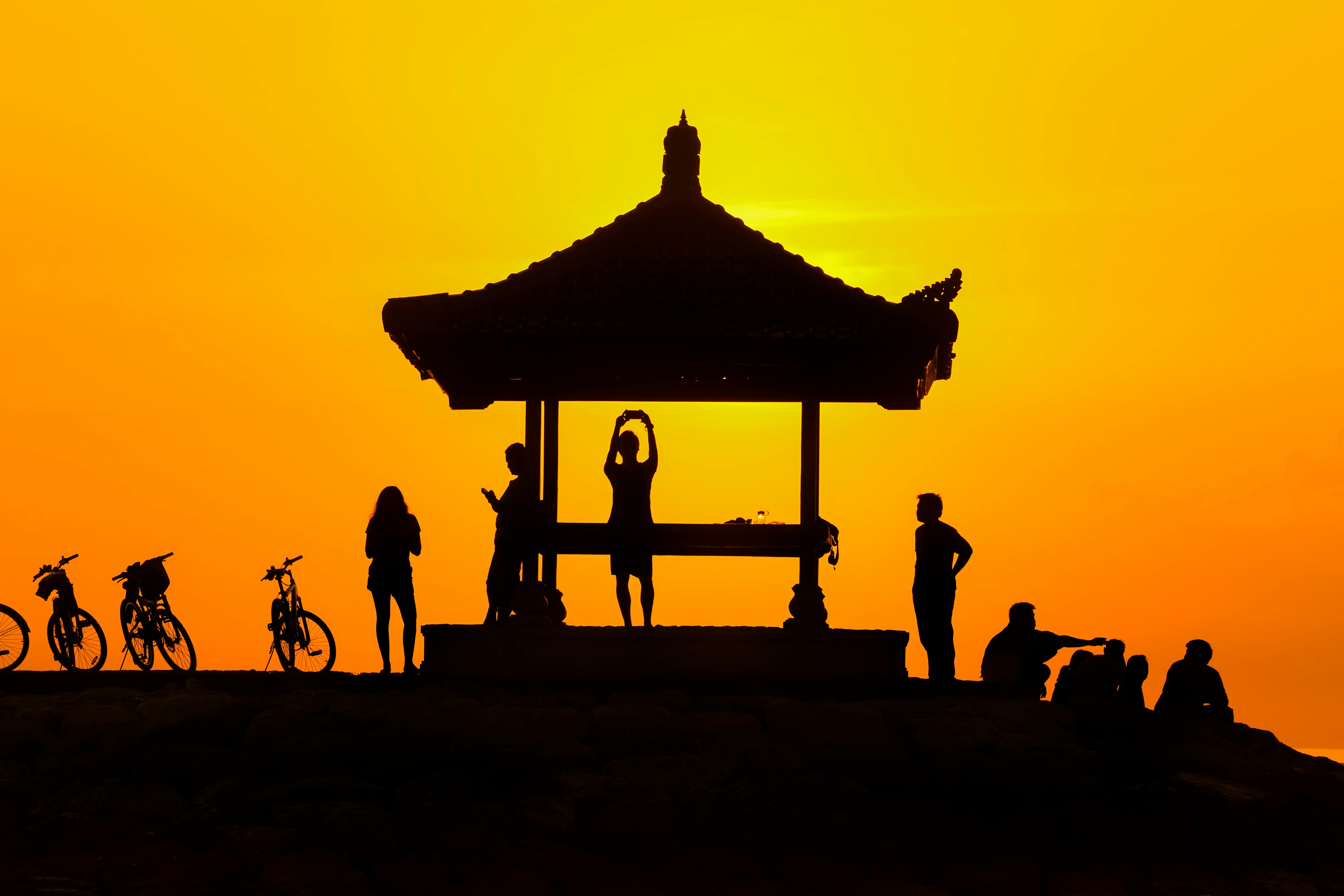 在充满活力的日落背景下，凉亭下的人们骑着自行车，剪影平静