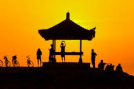 在充满活力的日落背景下，凉亭下的人们骑着自行车，剪影平静