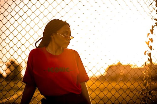 Wanita Dengan Kaos Leher Kru Konic Merah Berdiri Di Depan Pagar Wire Mesh