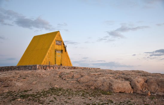 Yellow A-frame building on rocky terrain in Gerivan, Iran under a clear sky.