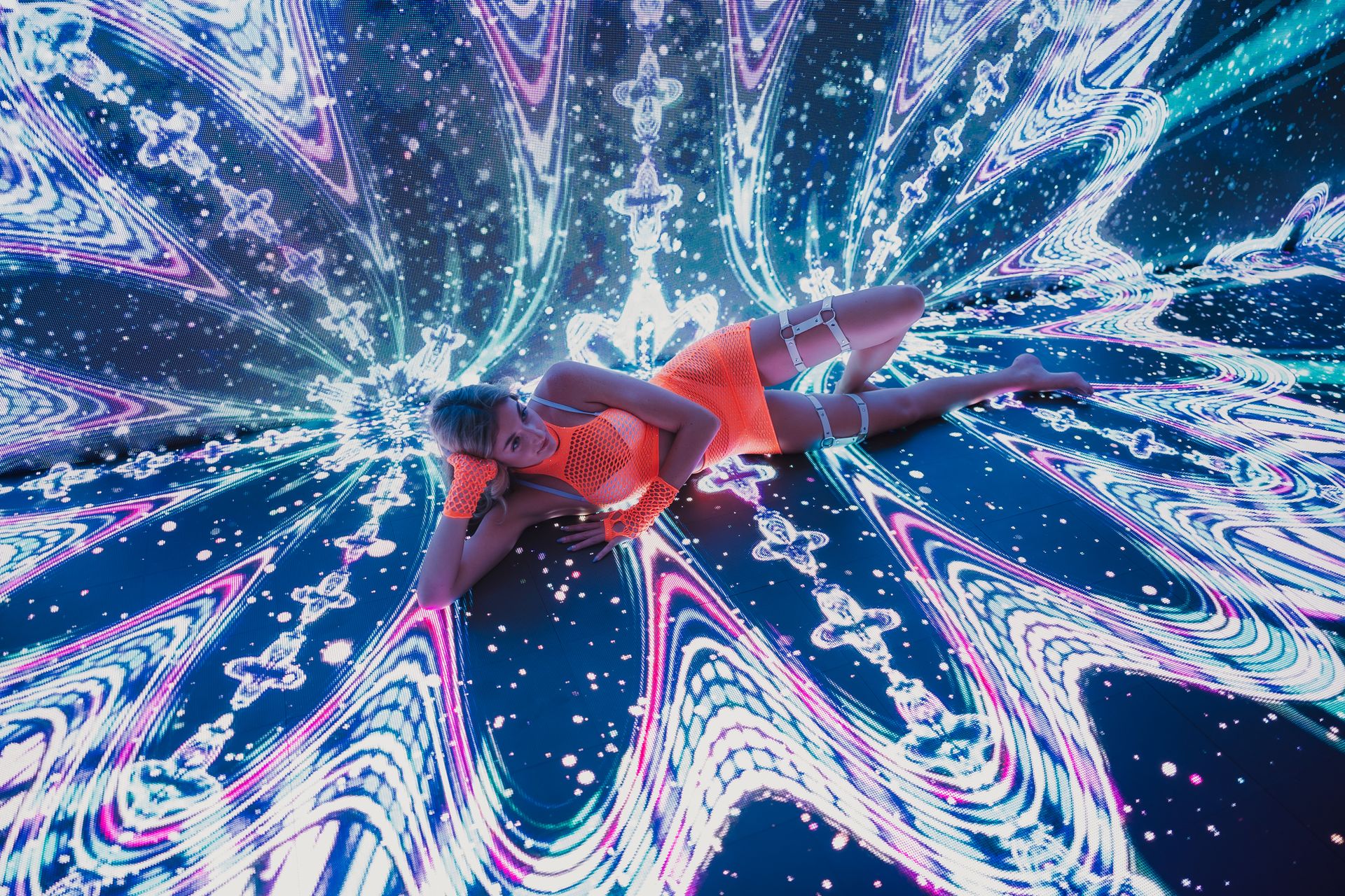 A dancer in vibrant neon attire performs on a digital stage with dynamic light patterns.