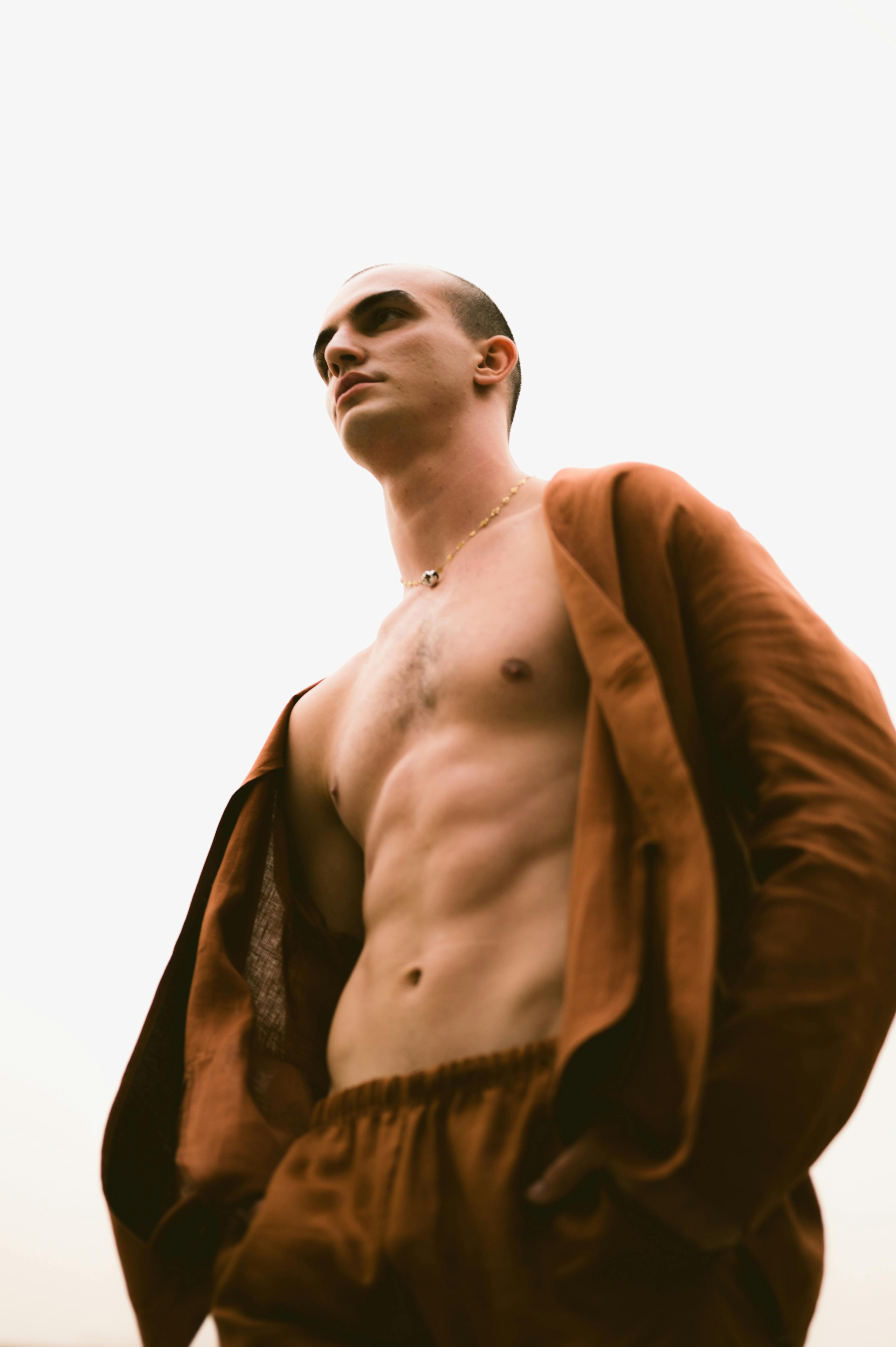 Man posing confidently in a brown outfit showcasing toned physique in an outdoor setting.