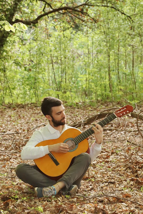 A man sitting in the woods playing an acoustic guitar