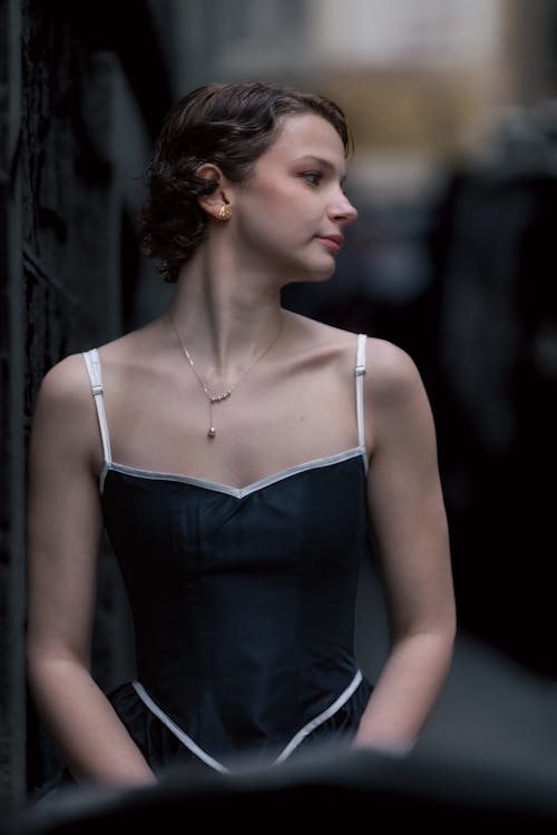 A woman in a black dress leaning against a wall