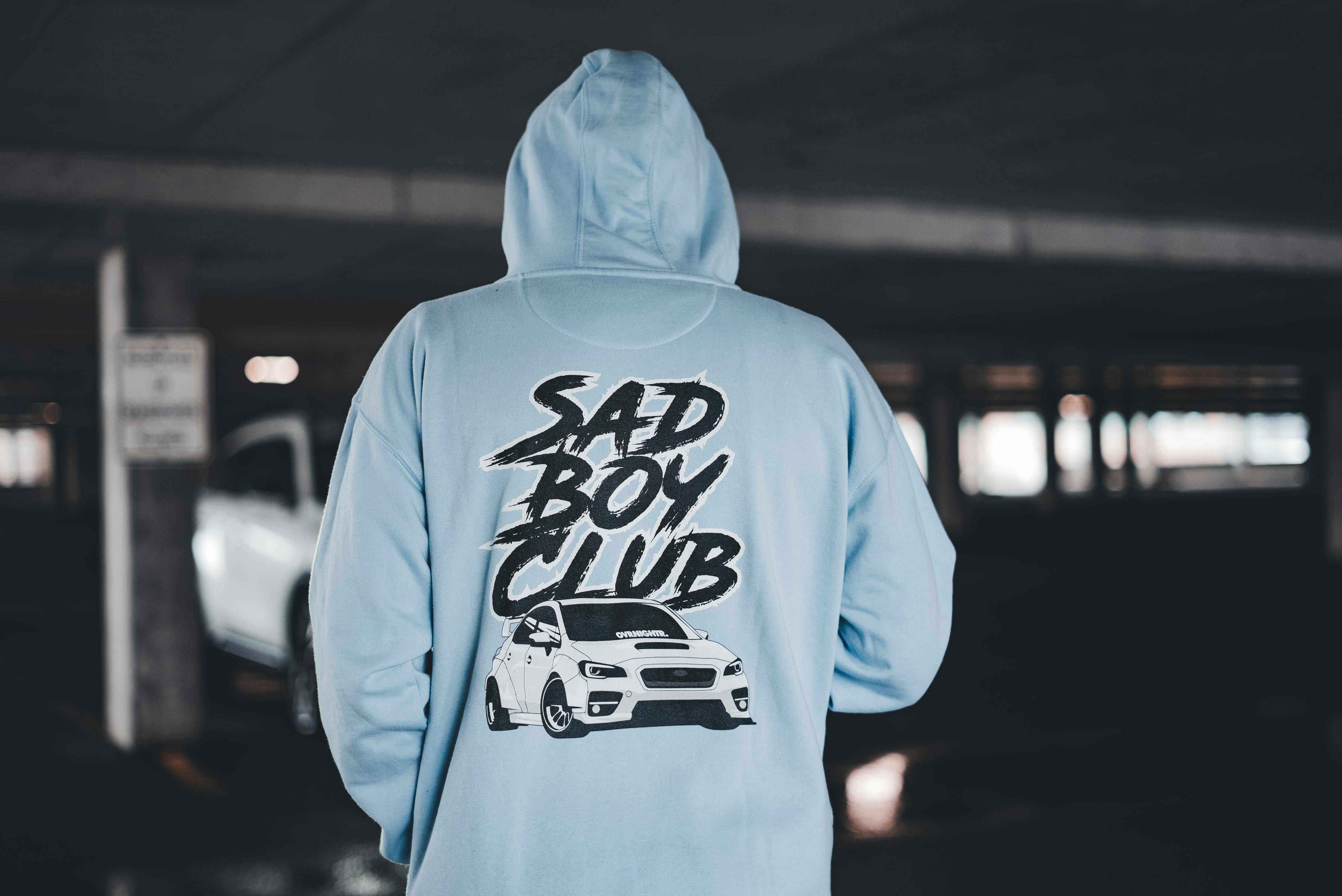 Person in Blue Hoodie with Sad Boy Club Script in Garage Free Stock Photo