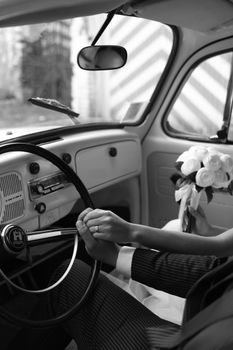 Black and white photo of a bride and groom holding hands inside a vintage car in Deutschland.