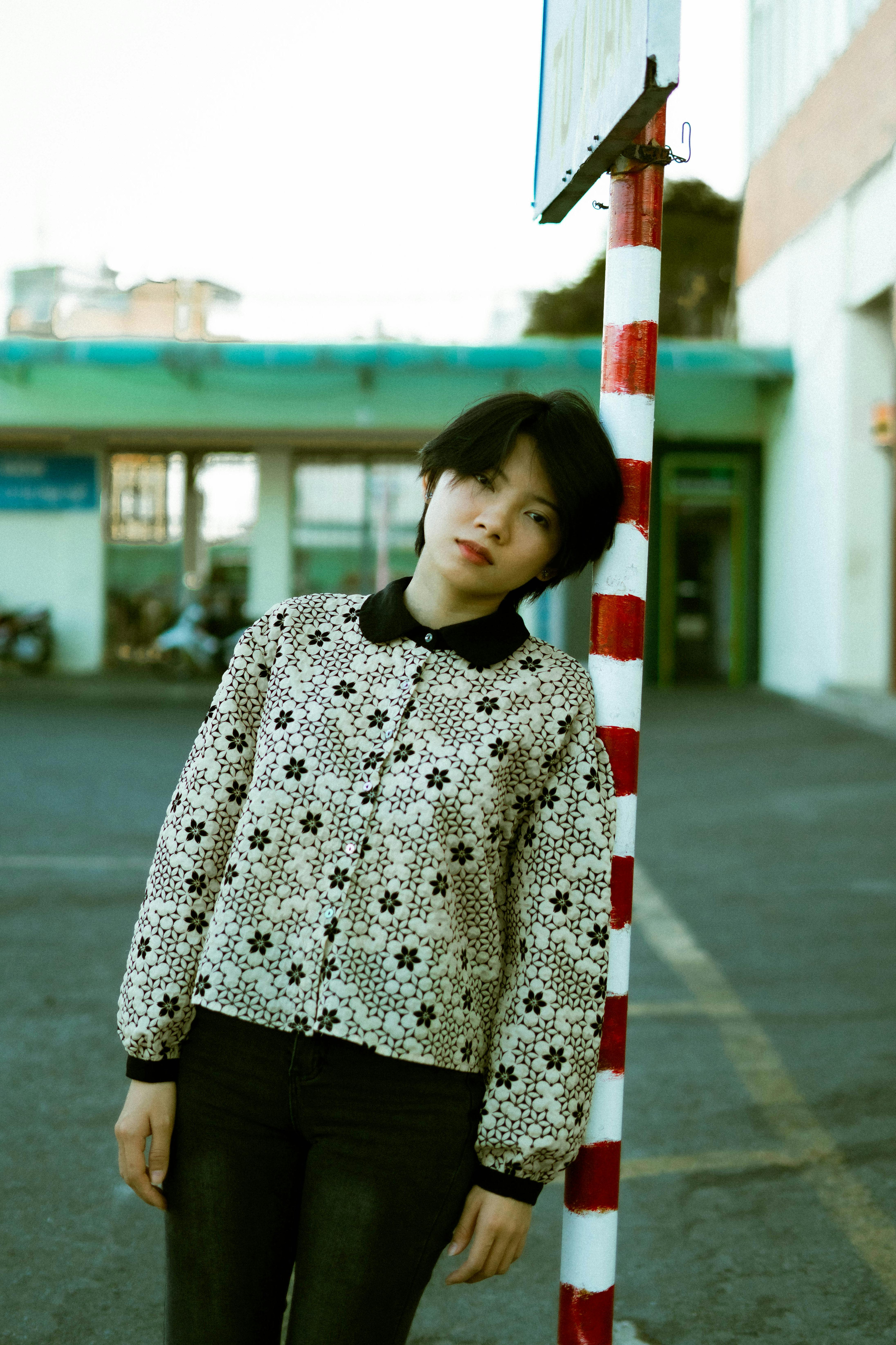 Young woman in trendy outfit stands in an urban setting, exuding serene confidence.