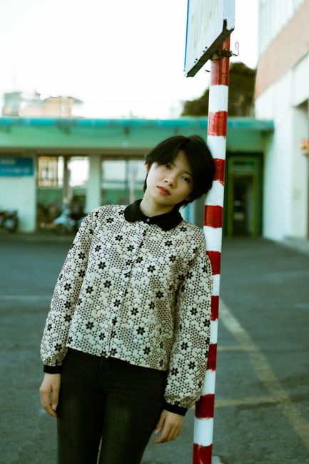 Young woman in trendy outfit stands in an urban setting, exuding serene confidence.