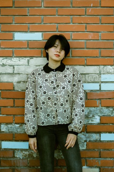 Fashion-forward woman posing against a rustic brick wall in a stylish patterned jacket.