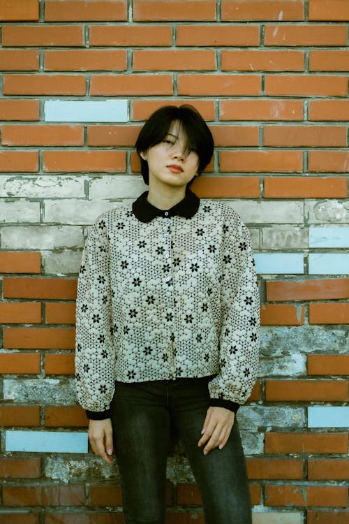 Free Young Woman in a Patterned Jacket Standing against a Brick Wall  Stock Photo