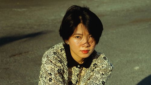 Free Young woman in fashionable patterned jacket sitting on sunlit city street. Stock Photo