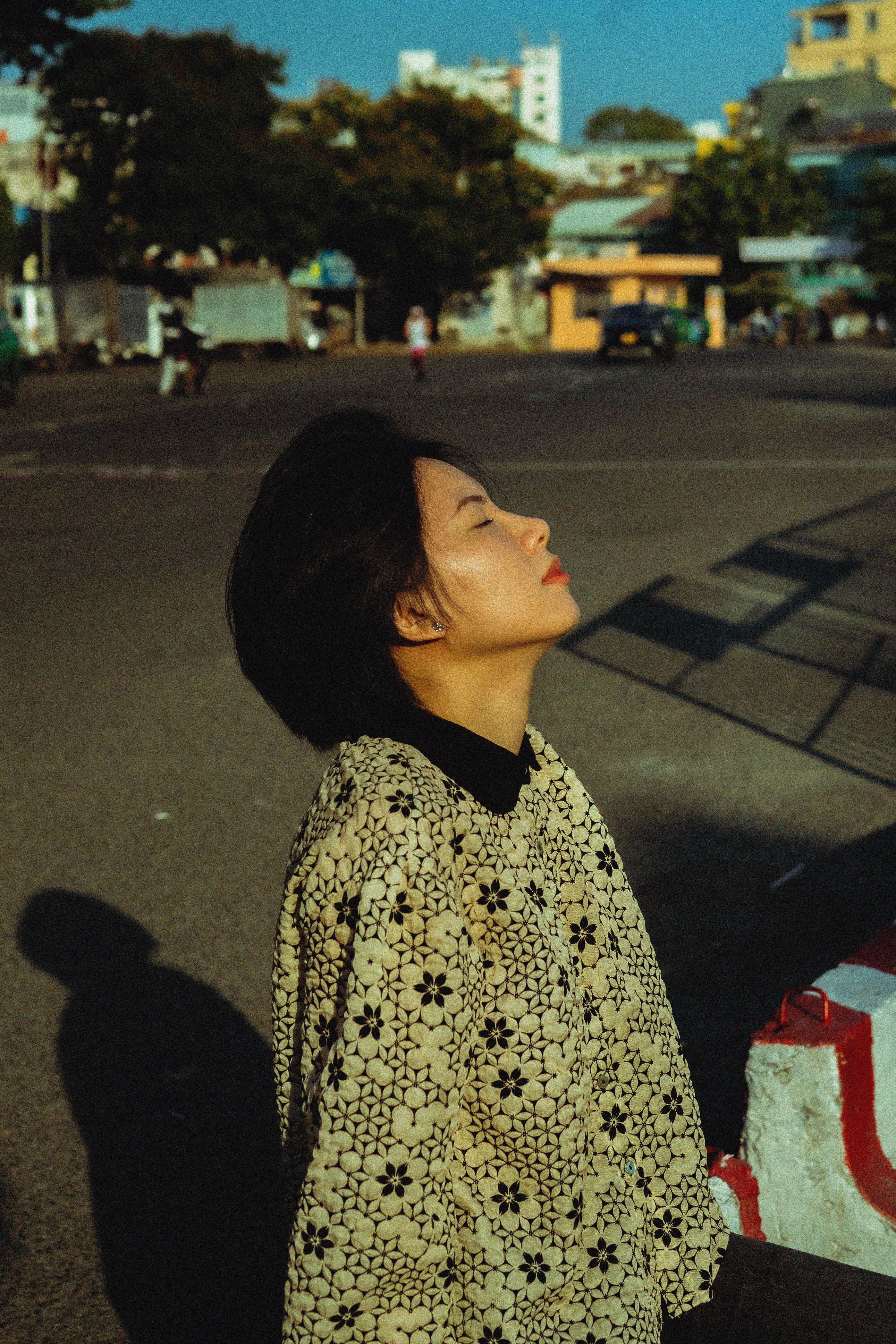 Woman enjoying sunlight in an urban setting with closed eyes and stylish clothing.
