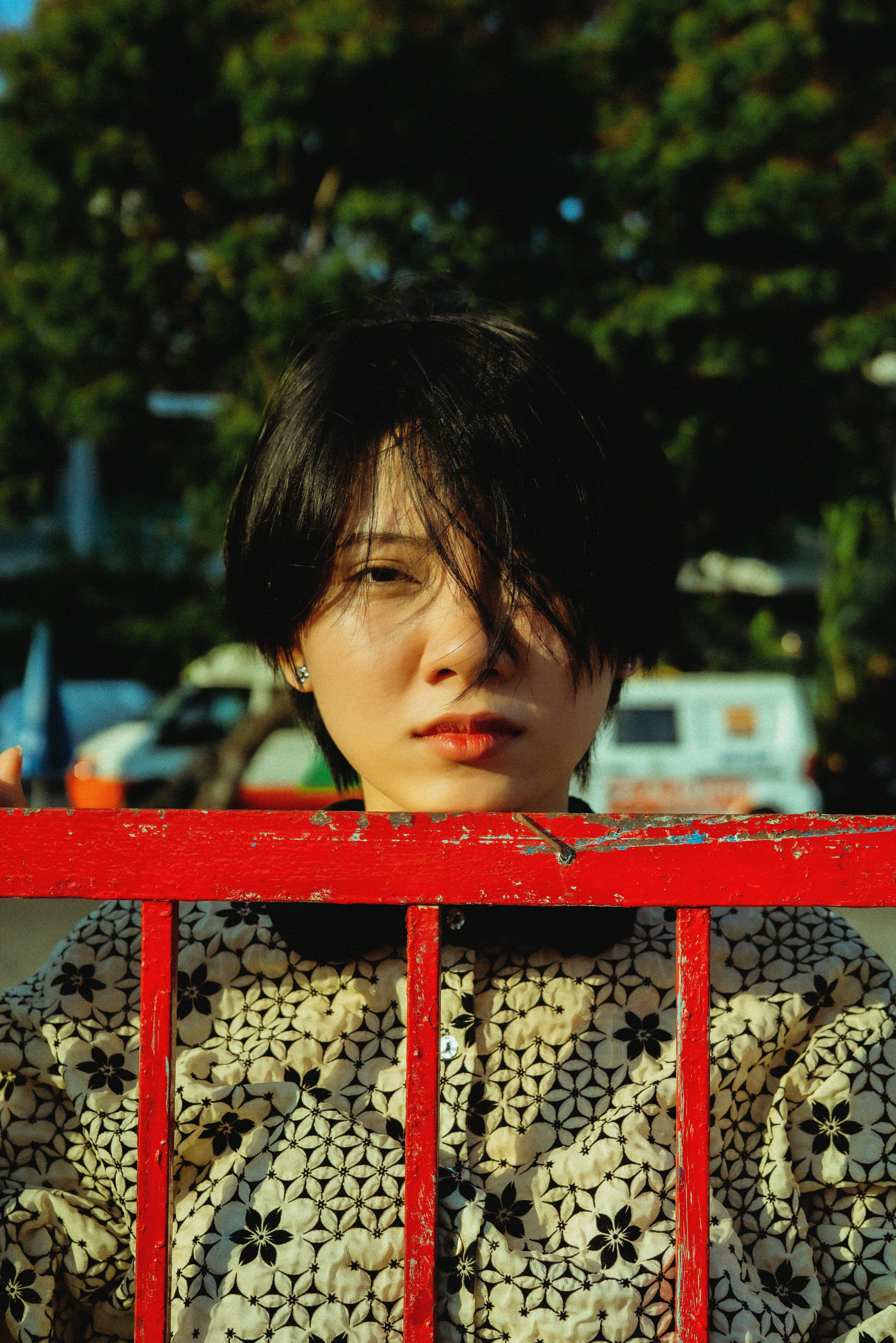 Stylish portrait of a young woman with short hair by a red fence in bright urban setting.