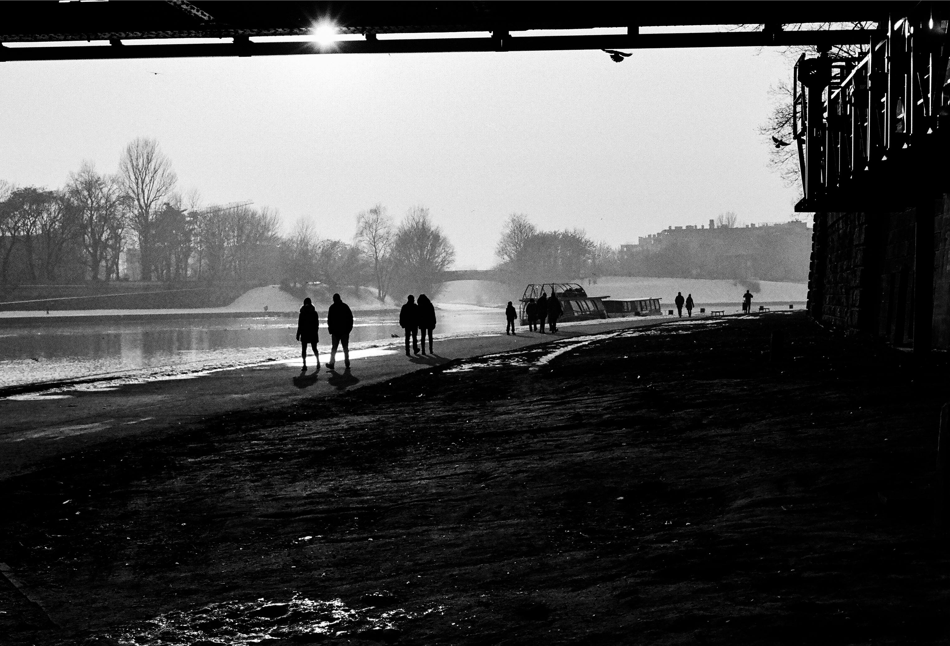 black and white photo of people walking along the river