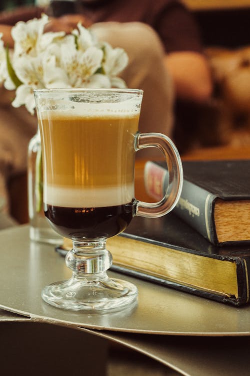 A glass of coffee sits on a table with books