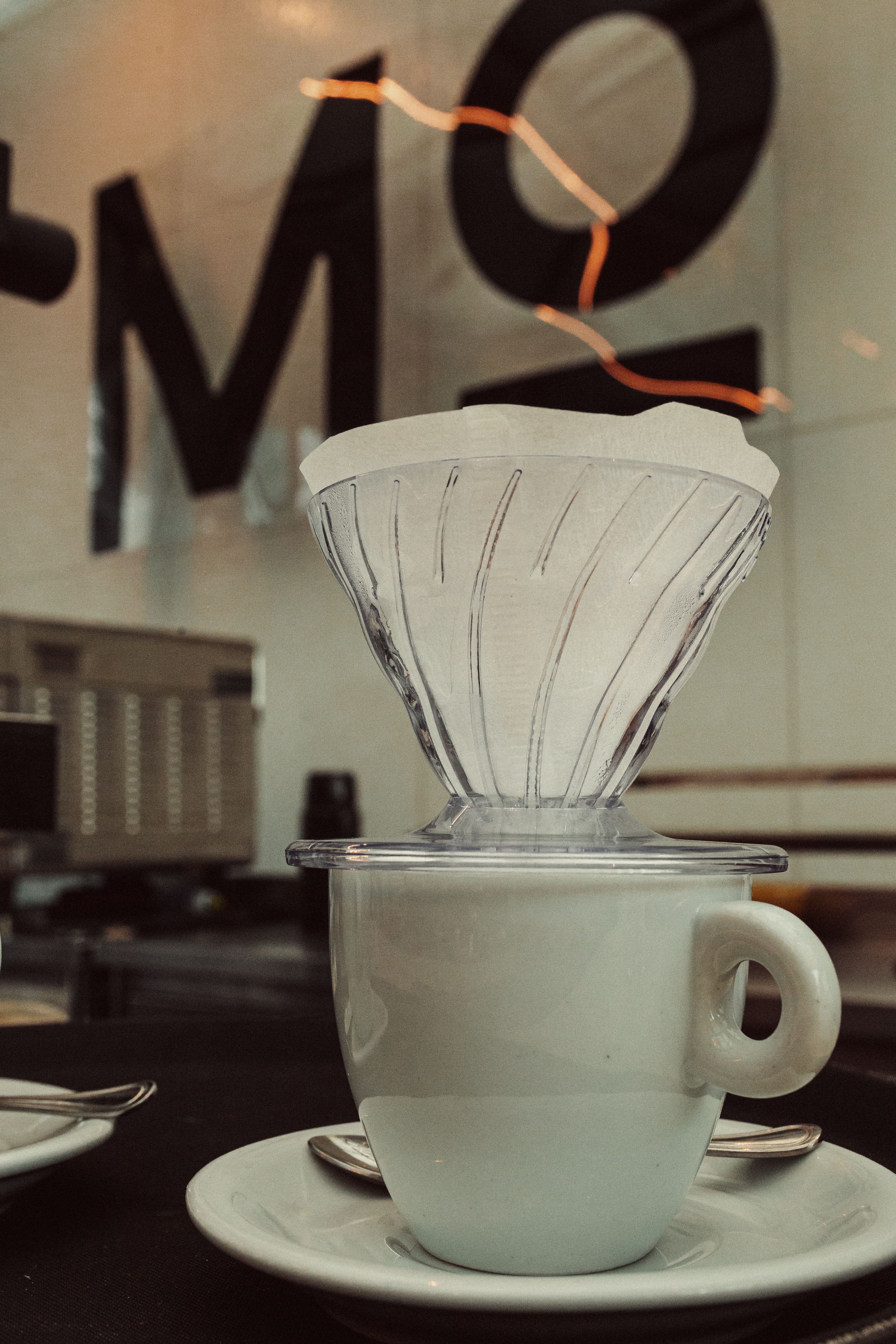 A modern coffee dripper atop a white cup in a trendy cafe setting.