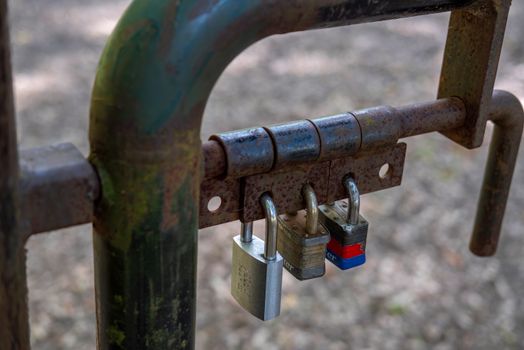 Close-up of a rusty gate secured with three padlocks, symbolizing security and protection.