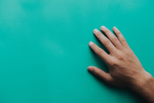 A man's hand placed on a teal surface, showcasing details and texture in a minimalist style.