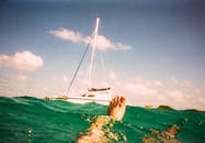 一个人漂浮在绿松石水附近的帆船下一个晴朗的天空