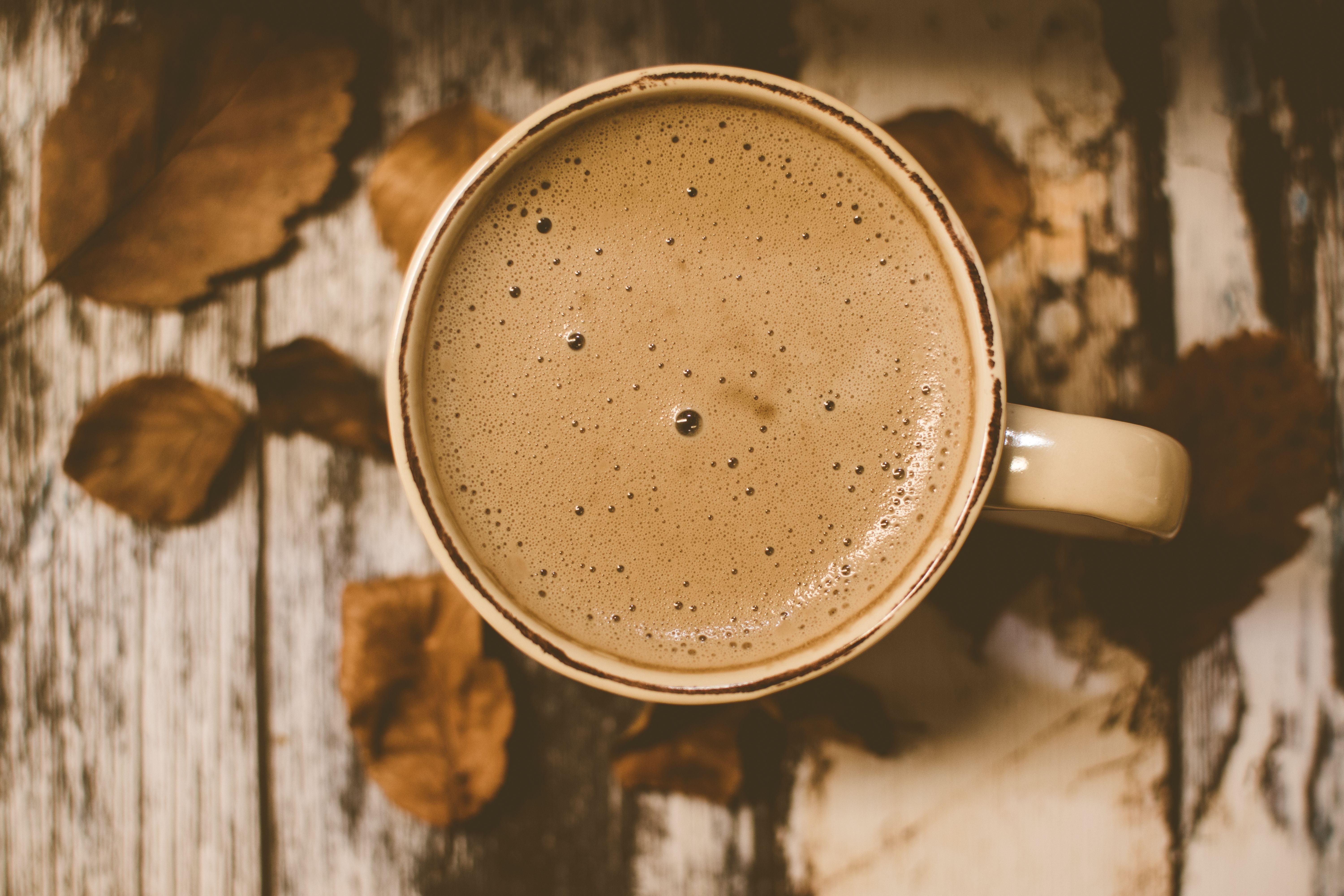 A rustic coffee mug sits on a wooden table surrounded by autumn leaves, creating a cozy atmosphere.
