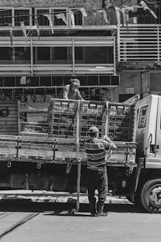 Two men working together to load a truck in the vibrant streets of Buenos Aires, captured in monochrome.