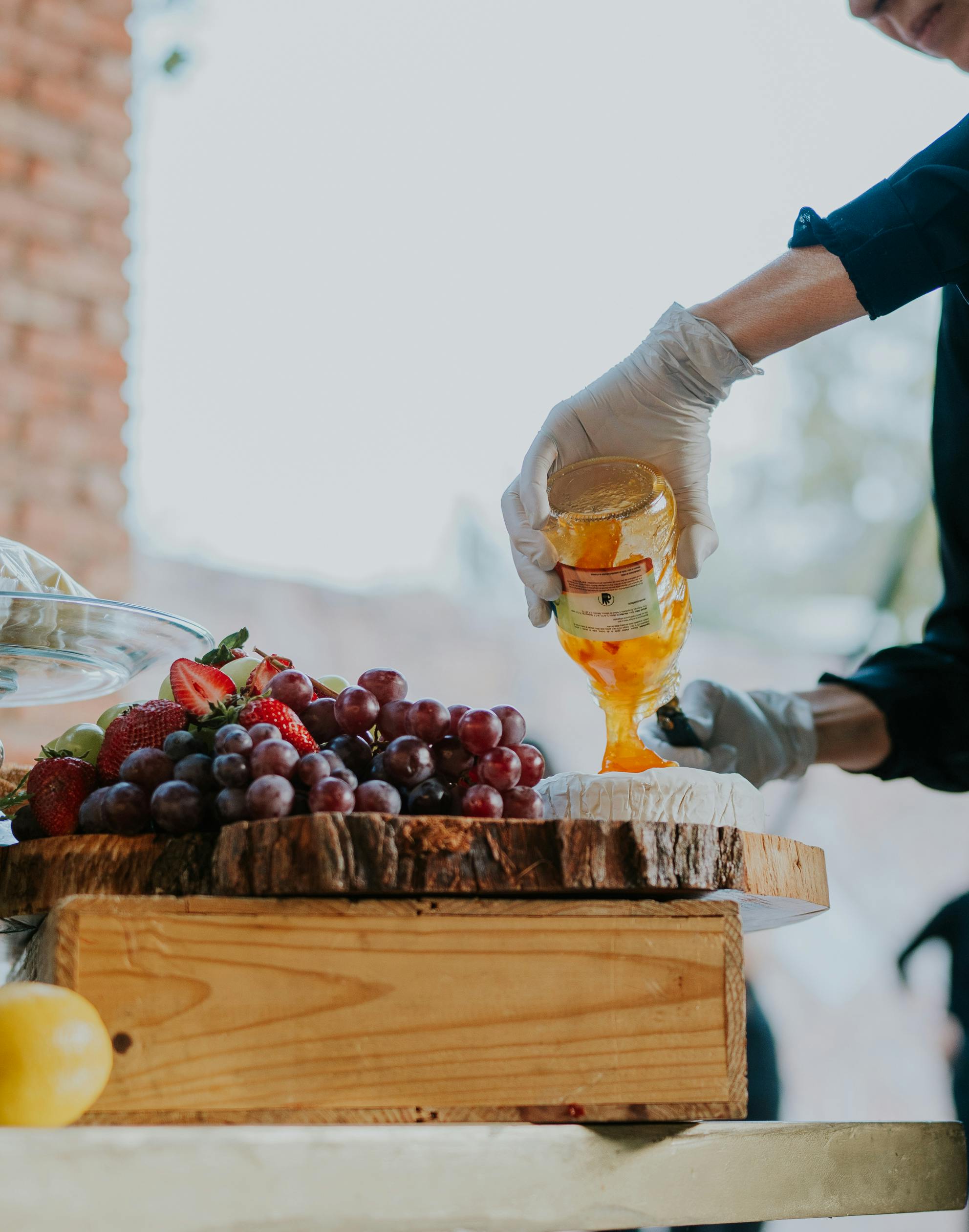 A person pours honey over cheese while preparing a fruit platter.